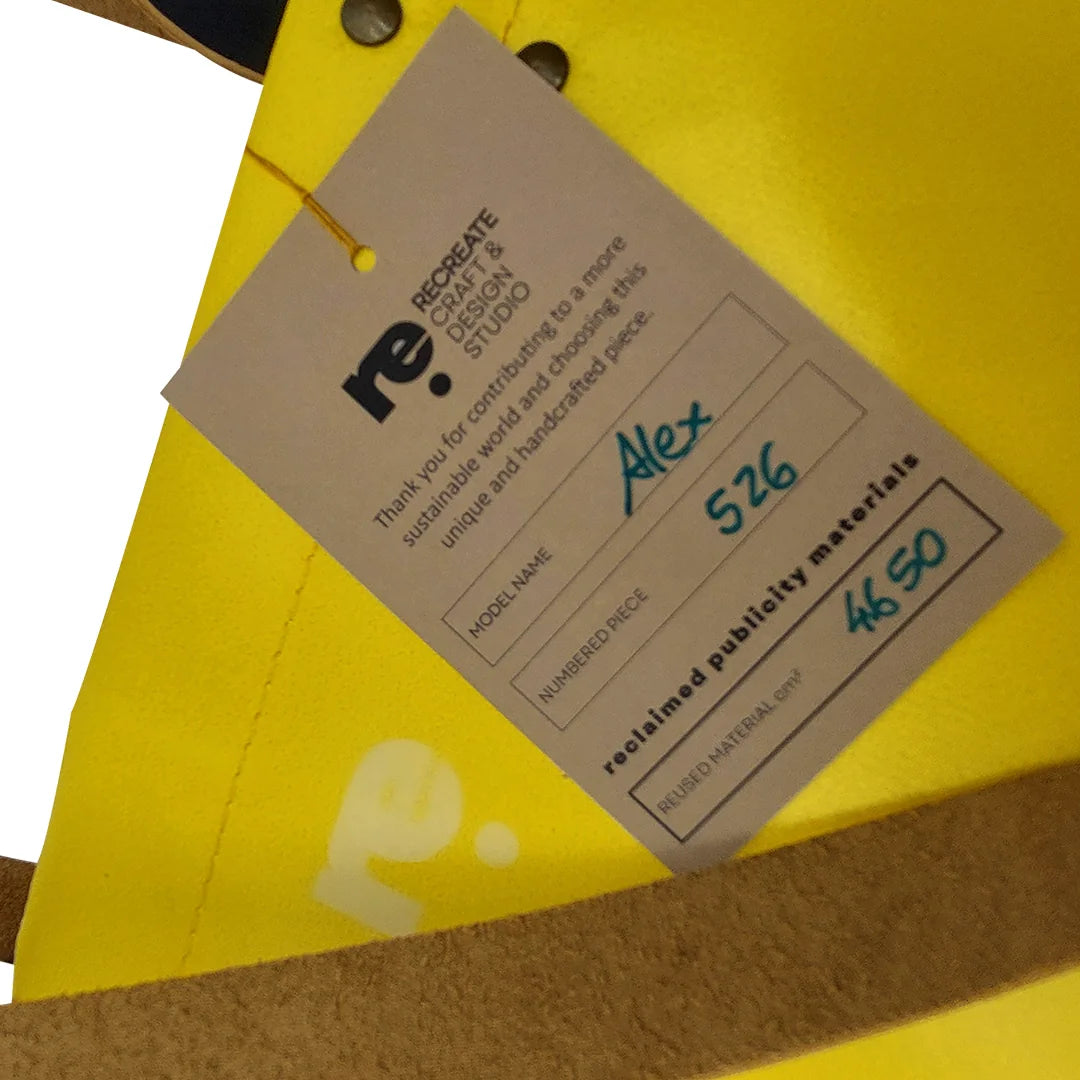 One-of-a-kind yellow and black handmade bag in reclaimed advertising banner, with leather handles and an inside pocket. Numbered ReCreate piece. - tag
