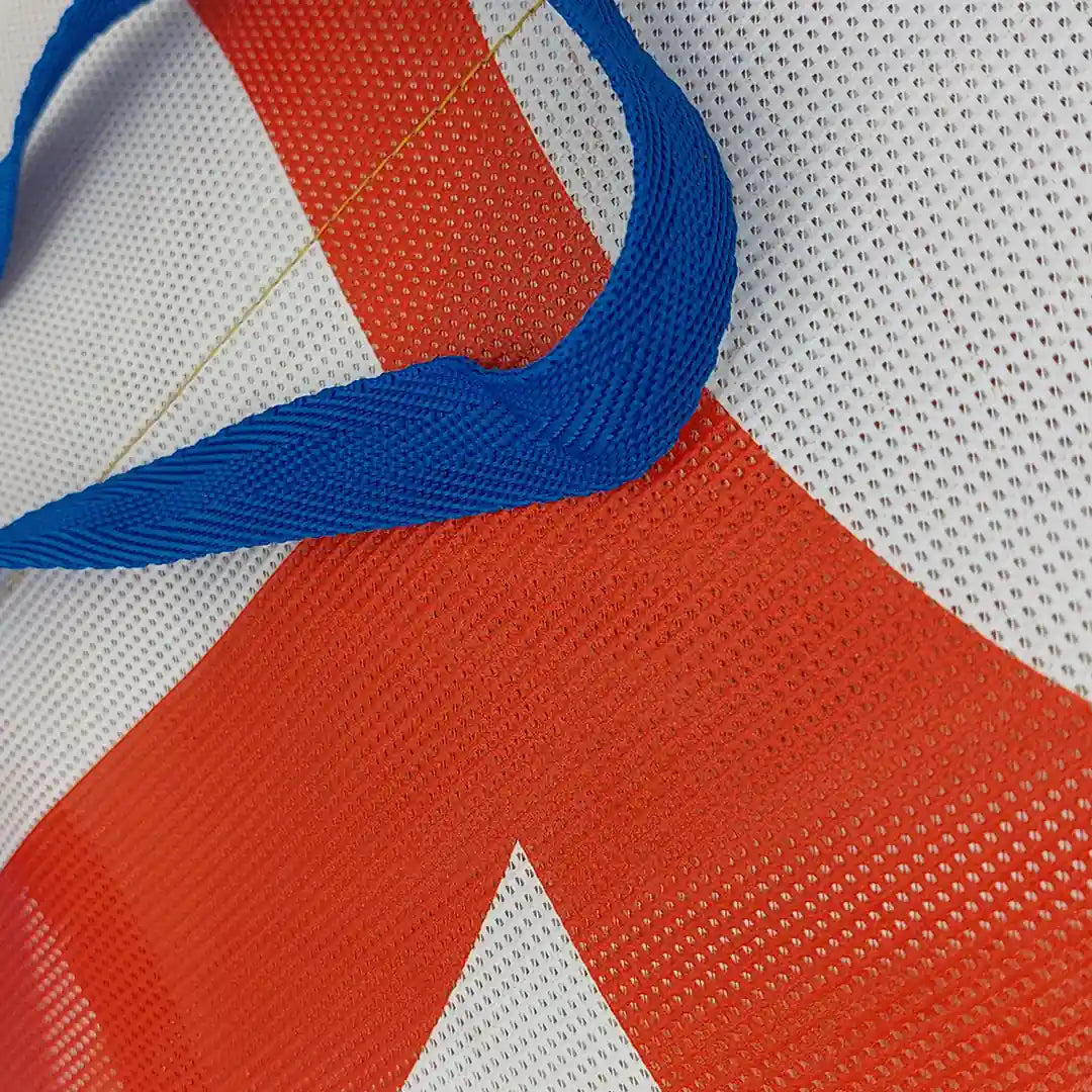 Red and white tote made from reclaimed advertising mesh banner, with blue handles and bold graphic curves from the original print. - detail