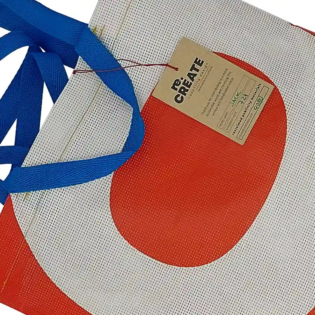 Red and white tote made from reclaimed advertising mesh banner, with blue handles and bold graphic curves from the original print. - tag