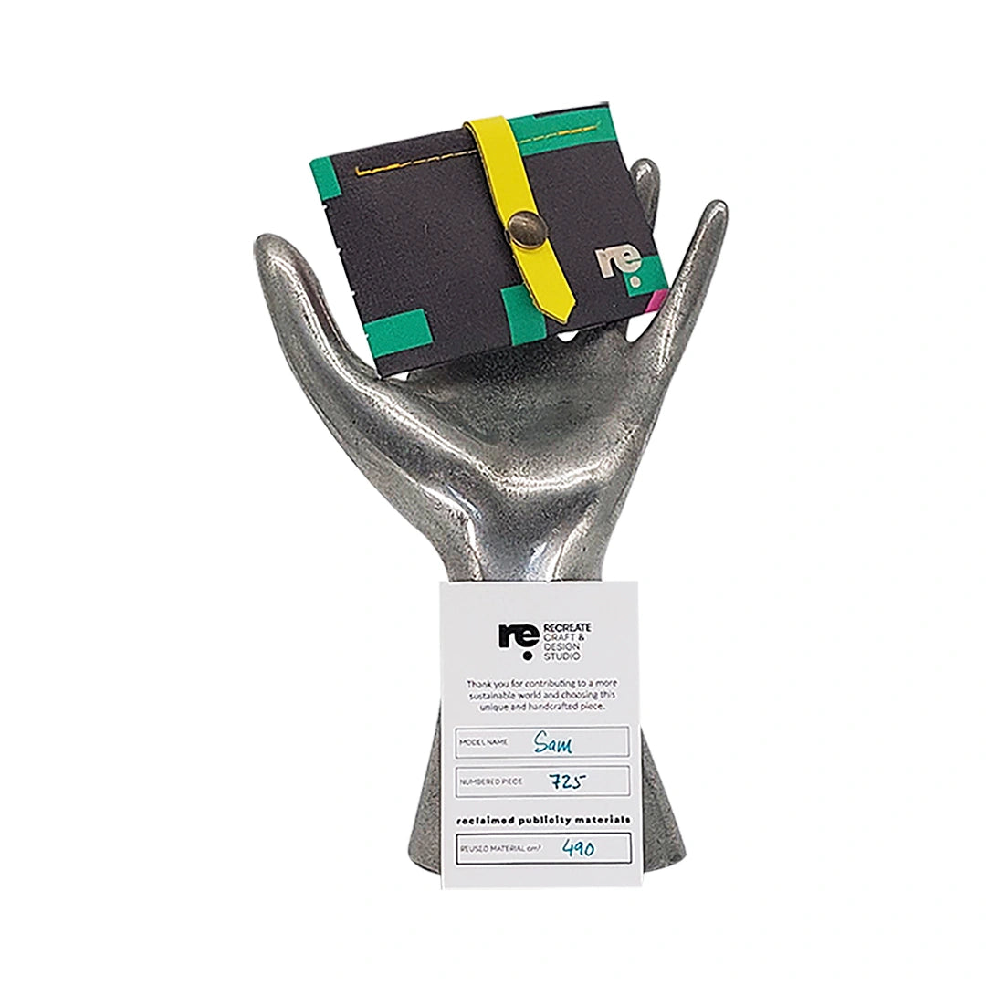 Sam Wallet 725 is a compact ReCreate wallet made from reclaimed advertising banner, with dark tones, vivid colour blocks and woven detail. - on hand